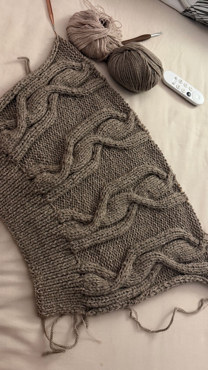 A cabled knit panel in progress, with two balls of yarn